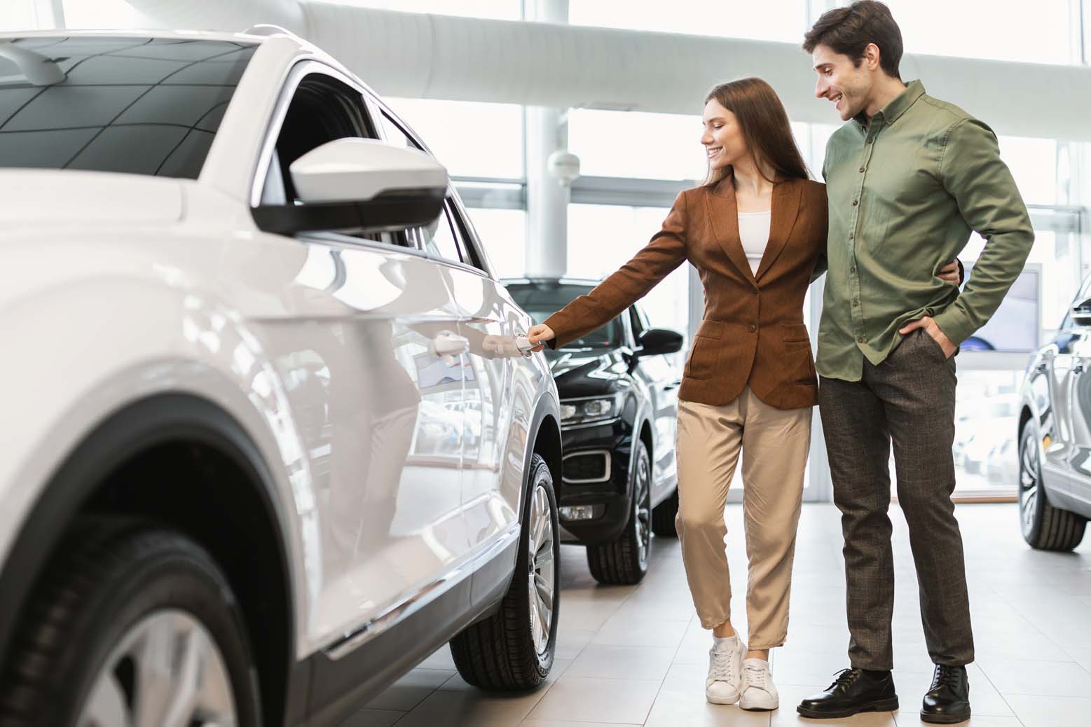 Young couple examines new cars in a car dealership.