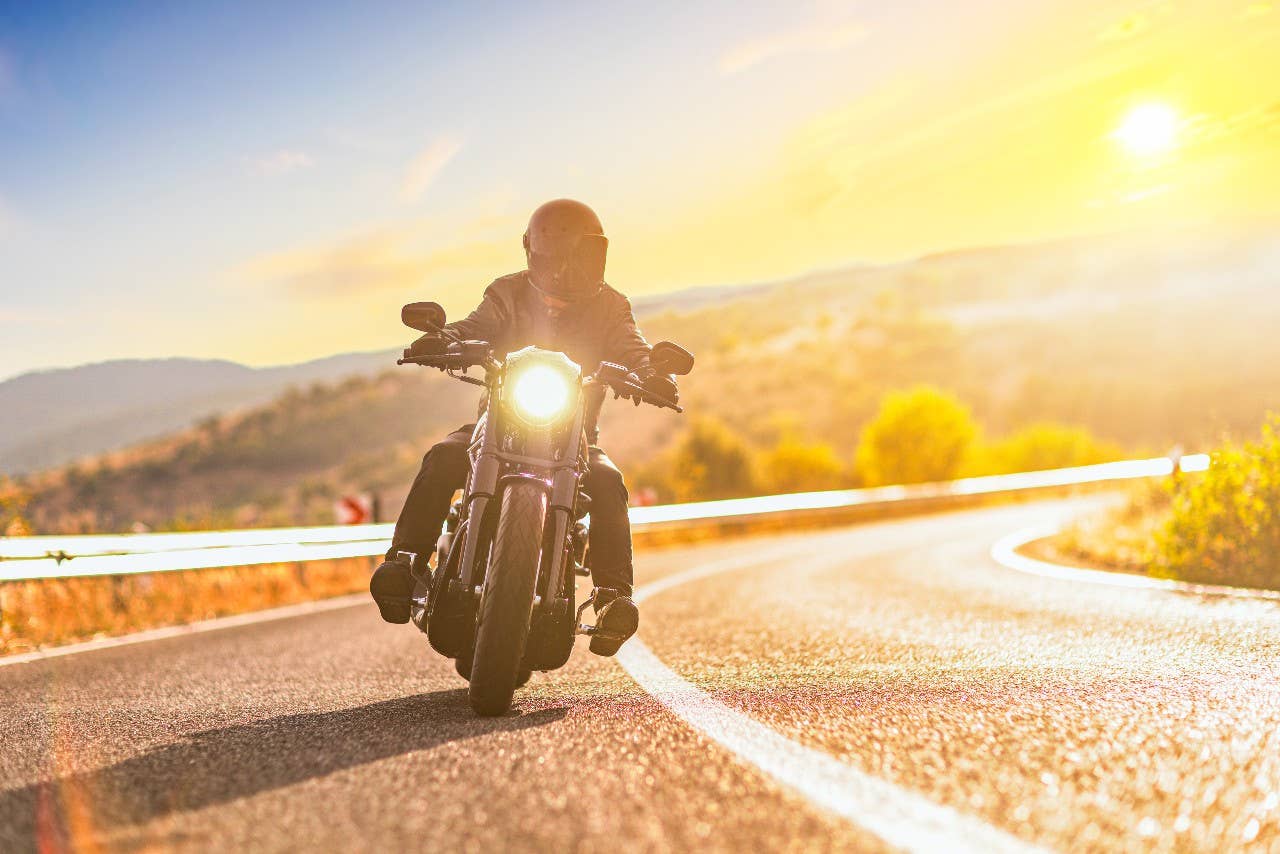 Sunset over an open road and a man with a helmet riding a chopper motorbike